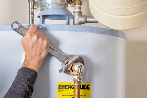 A person uses a wrench to adjust a pipe on top of a water heater with an Energy Guide label.