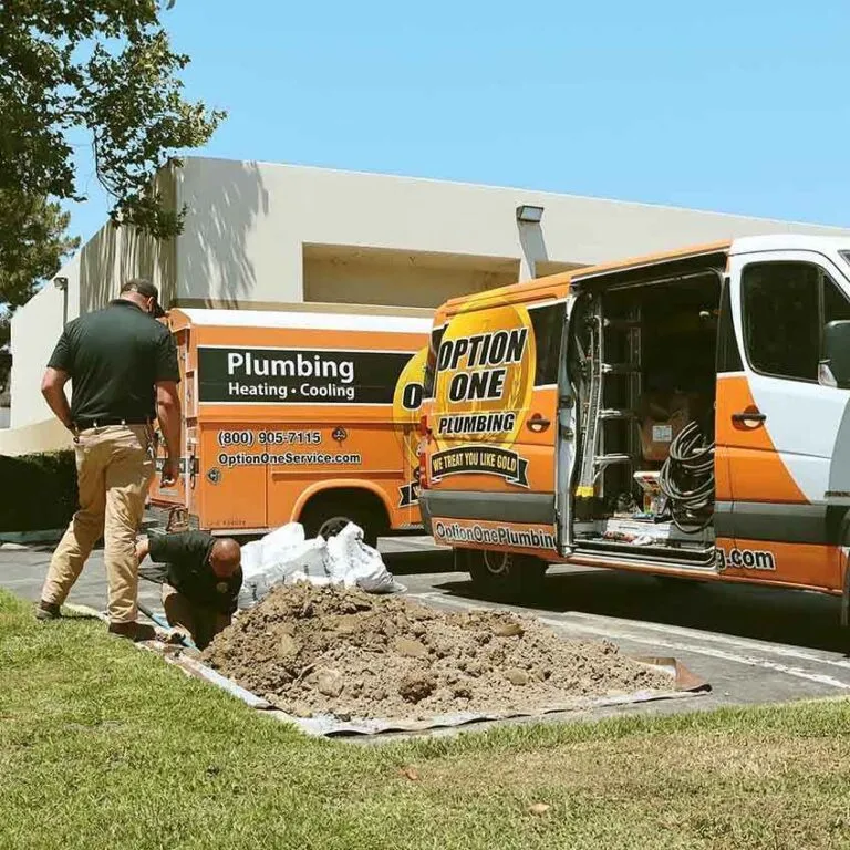 Two plumbers work near an open trench with soil piled beside two Option One Plumbing vans parked on a sunny day, showcasing the hands-on careers available.